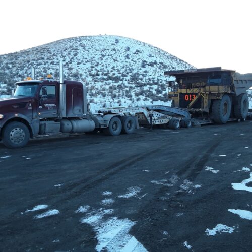 A heavy-duty truck hauling a large mining vehicle on a snowy landscape, highlighting transportation logistics in mining operations.