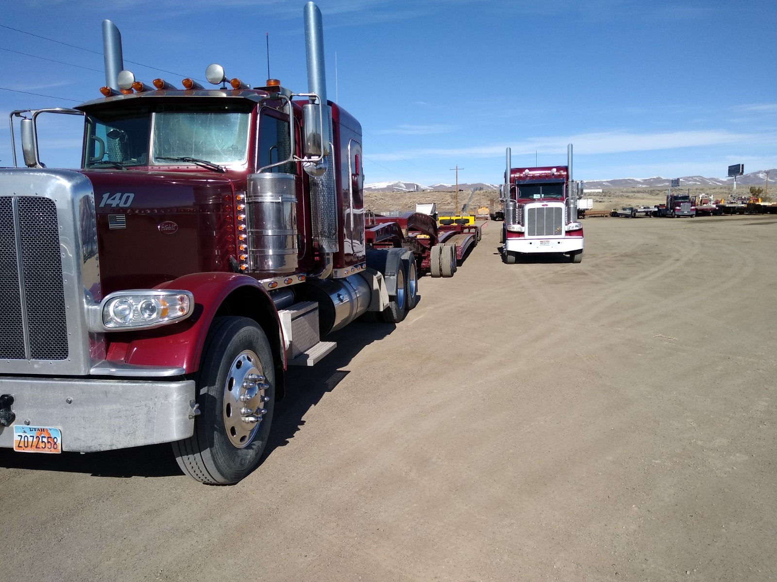 Two large, red semi-trucks parked on a dirt lot under a clear blue sky, highlighting their sleek designs and chrome details.